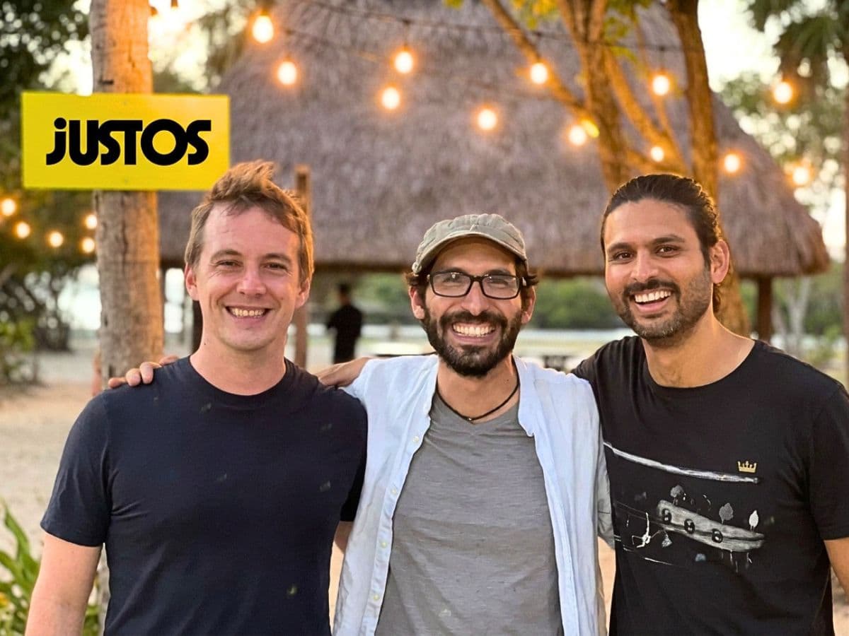Dhaval Chadha, Antonio Molins e Jorge Soto Moreno, fundadores da Justos, ao lado do logotipo da empresa