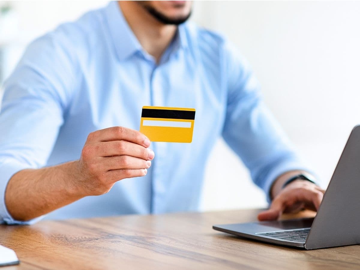 Pessoa fazendo pagamento online com cartão de crédito ao lado do notebook